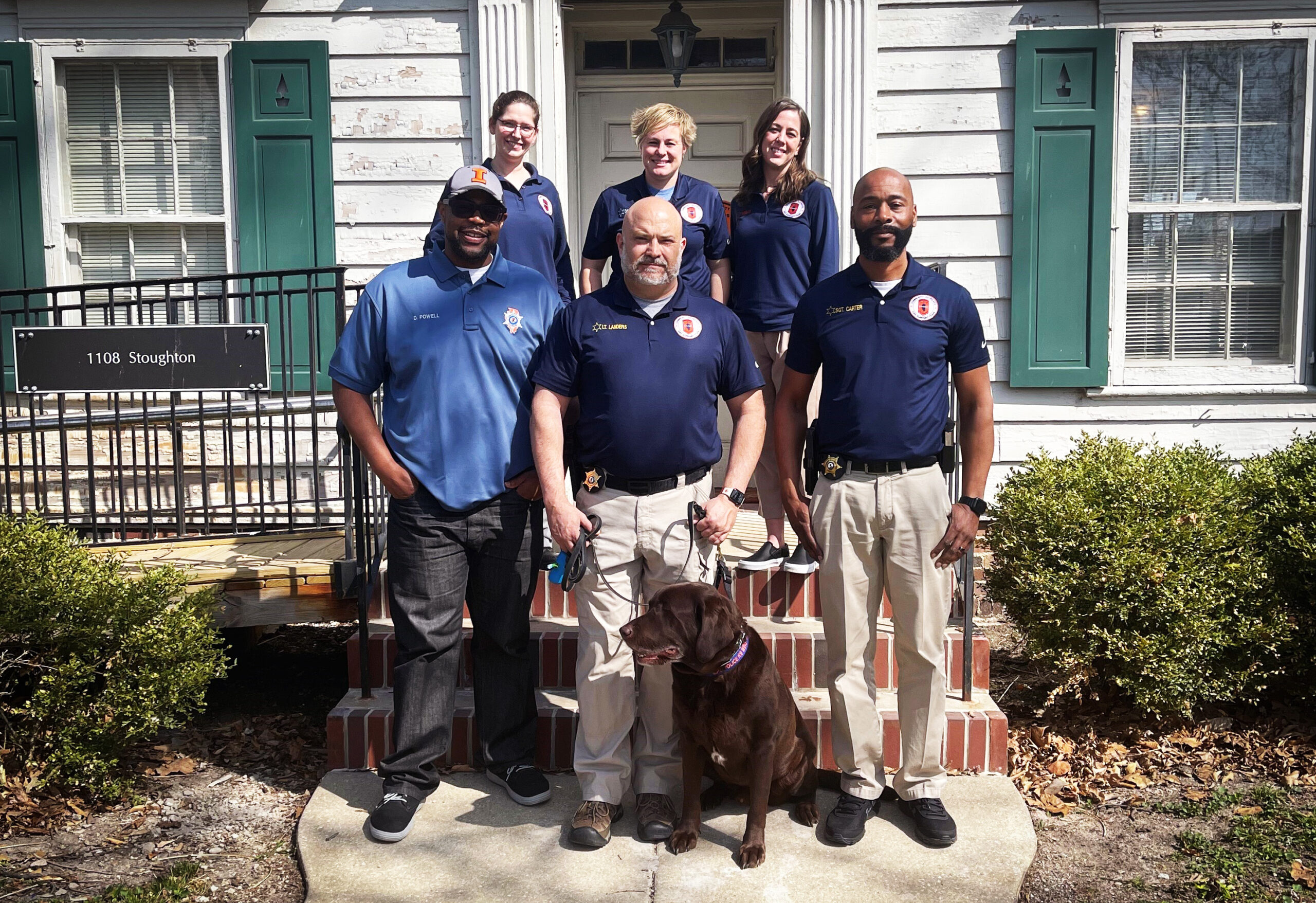 Six COAST team members and a dog pose for a photo on the front steps of the house where they work.