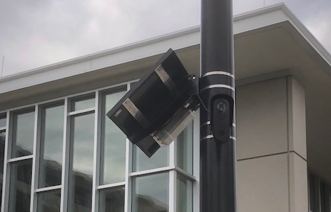 Camera and solar panel strapped to a post in front of a campus building