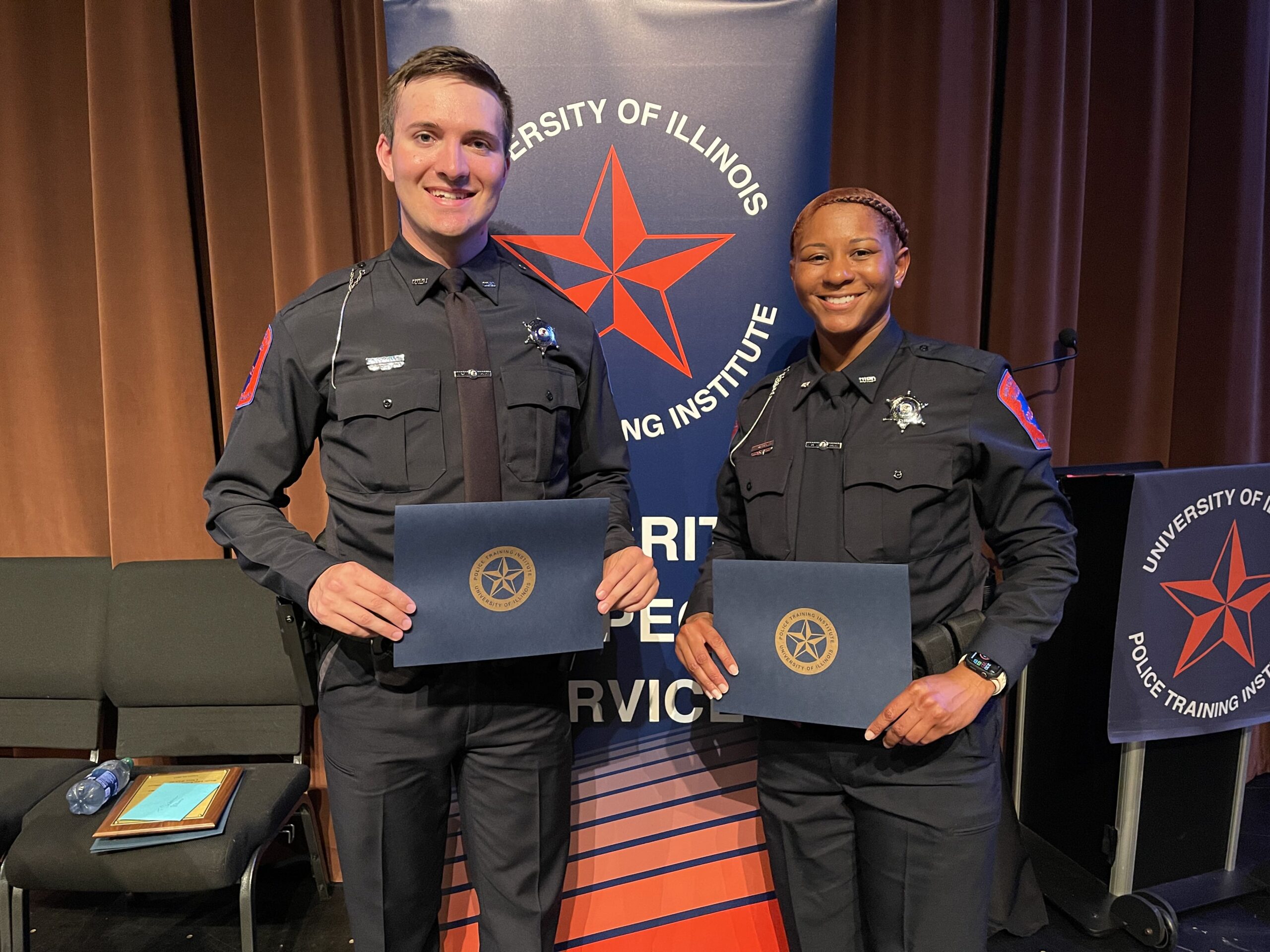 Two police officers pose for a photo with certificates