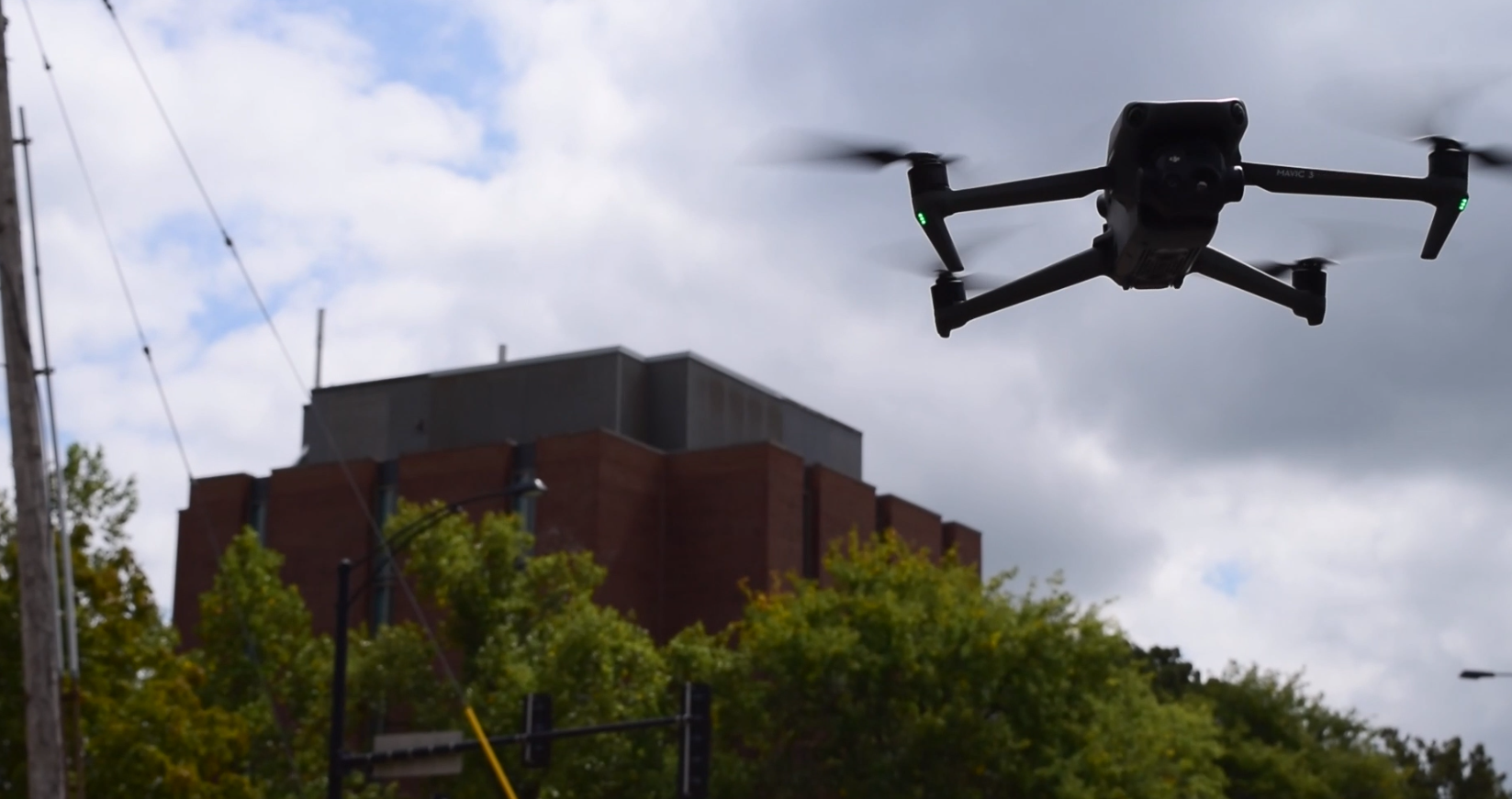 Airborne drone against a cloudy background. A campus building and trees are also visible.