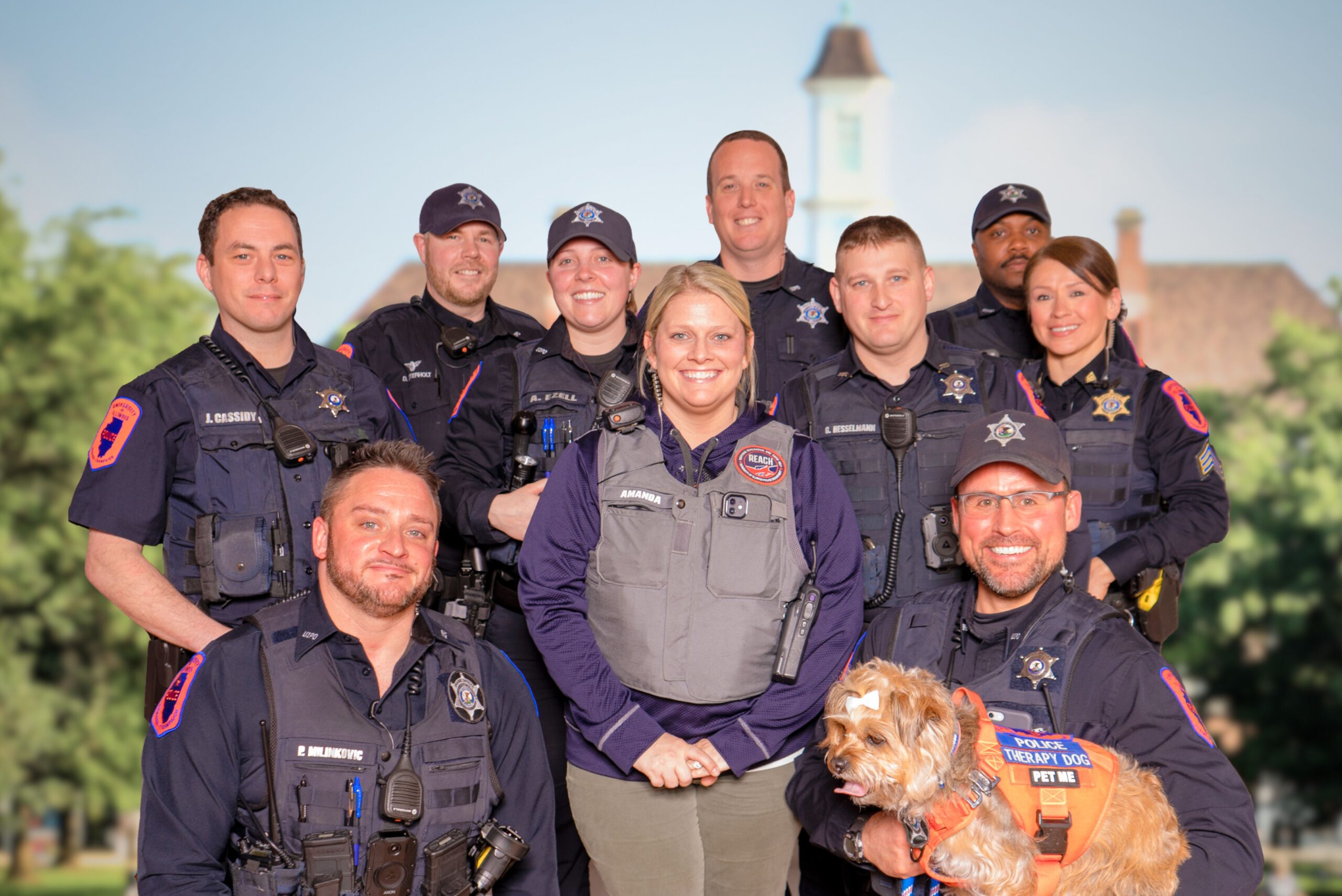 A smiling group of Division of Public Safety employees pose for a photo with the Illini Union in the background.